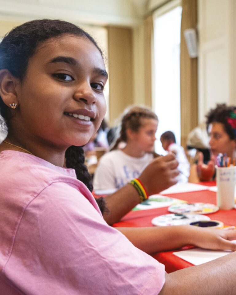 A girl in a pink t-shirt looking at the camera engaging in craft activities.
