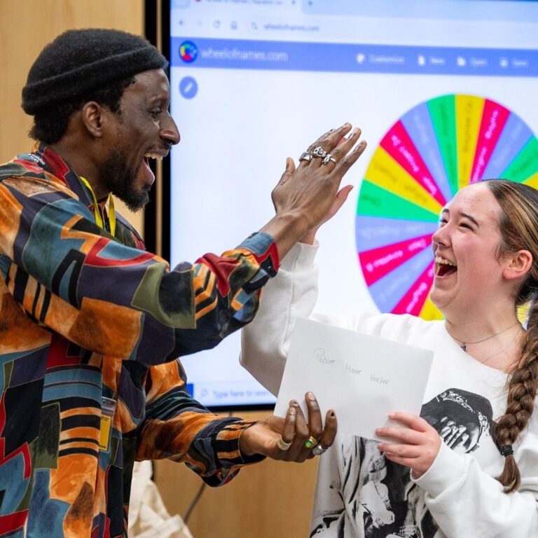 A man giving a woman a high-five in front of a powerpoint presentation. Both are laughing.